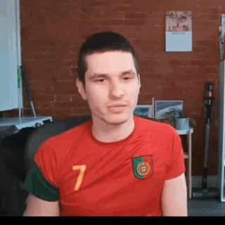 a man wearing a red shirt with the number 7 on it is sitting in front of a brick wall .