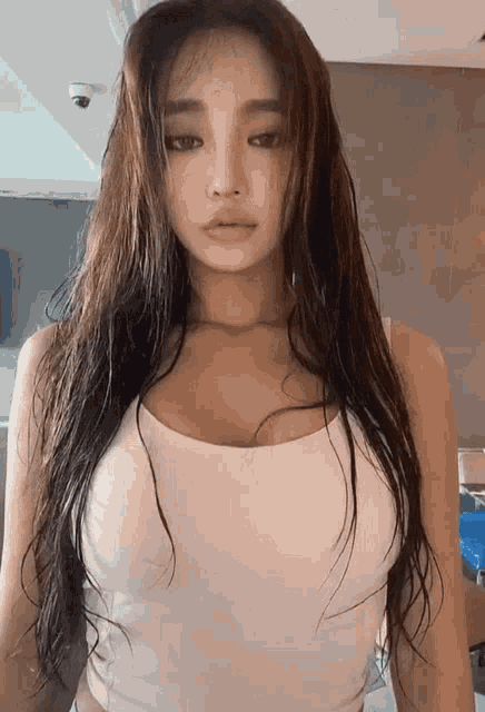 a woman with long hair is wearing a white tank top and looking at the camera