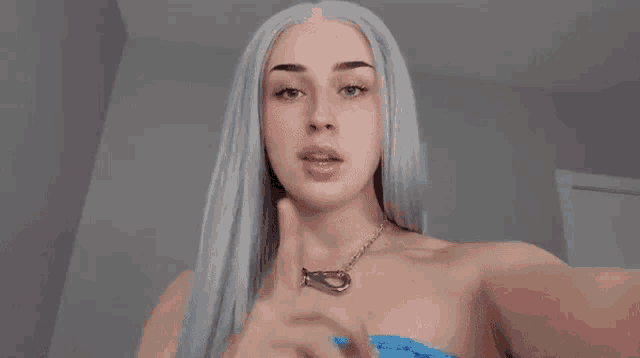 a woman with long white hair is holding her finger to her mouth .