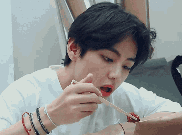 a young man is eating something with chopsticks while wearing many bracelets