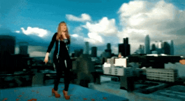 a woman stands on a rooftop with a city skyline in the background