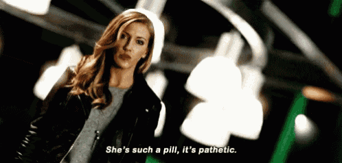 a woman in a leather jacket is standing in a dark room and talking about a pill .