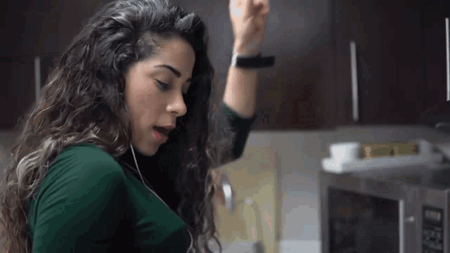 a woman in a green shirt is listening to music in a kitchen
