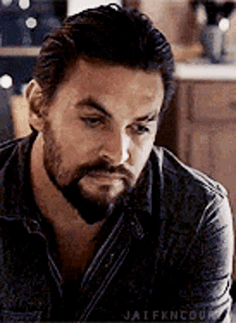 a man with a beard and mustache is sitting in a kitchen looking down .