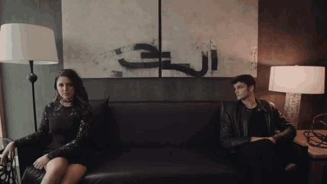a man and a woman are sitting on a couch in front of a painting that says ' arabic '