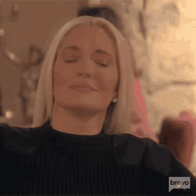 a woman with her eyes closed is wearing a black sweater and sitting in a chair .