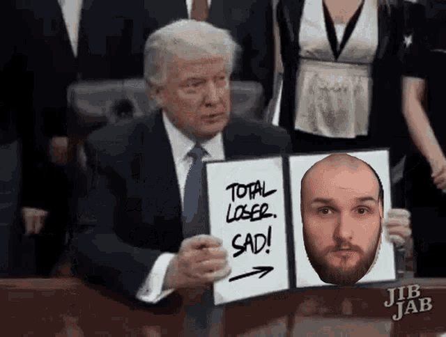a man in a suit and tie holds a sign that says total loser sad