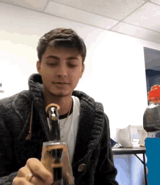 a young man in a black sweater is smoking a bong