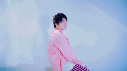 a young man in a pink shirt is sitting on a couch with his arms outstretched