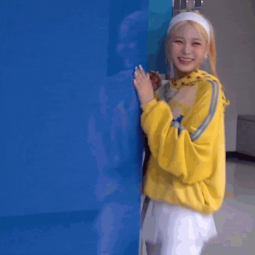 a woman wearing a yellow jacket and a headband is standing in front of a blue wall .