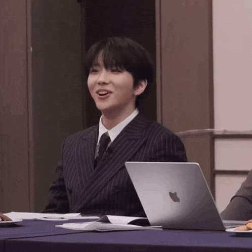 a man in a suit sits at a table with an apple laptop on it