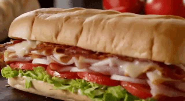 a sub sandwich with ham , bacon , lettuce , tomatoes and cheese on a bun .