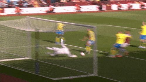 a blurry picture of a soccer game with a goalie diving to save the ball