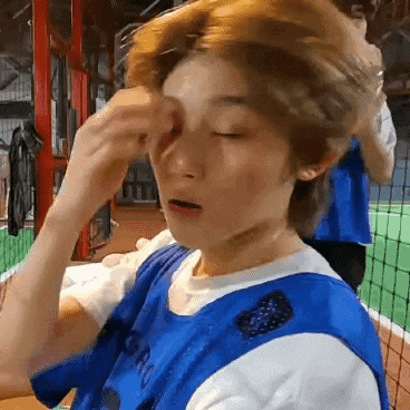 a person in a blue and white shirt is rubbing their face .