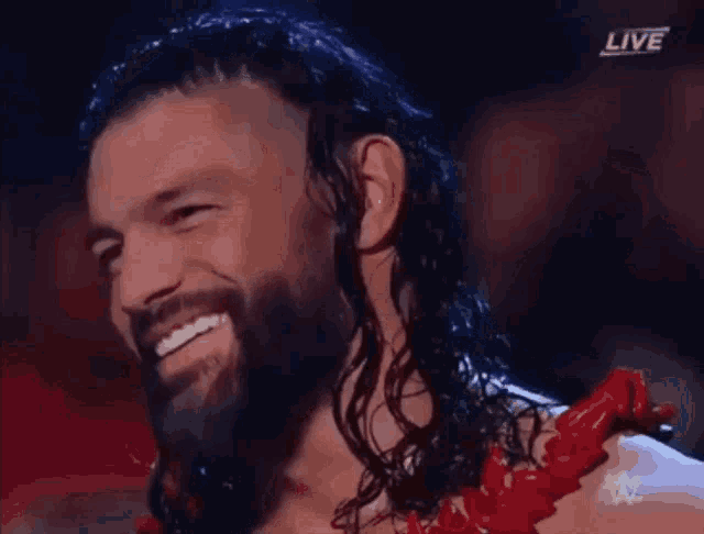 a man with long hair and a beard is smiling in front of a screen that says live