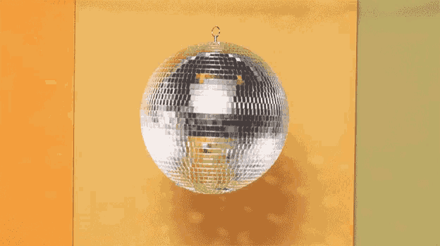 a disco ball is hanging from a hook on a yellow wall .