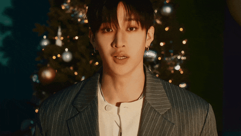 a young man in a striped suit stands in front of a christmas tree