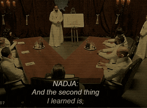 a woman sits at a table with two men and says " as a woman sometimes you do need " at the bottom