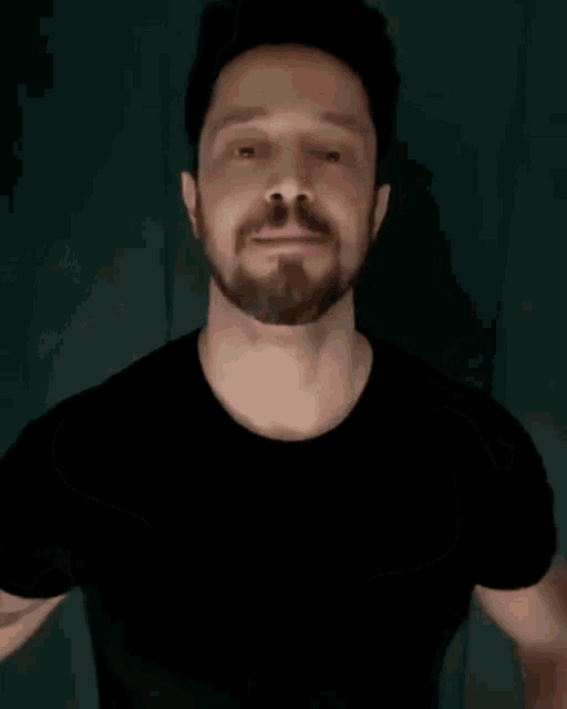 a man with a beard is wearing a black shirt and making a hand gesture .