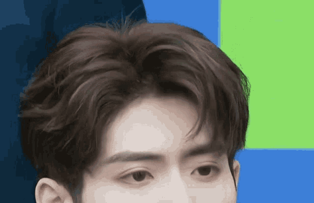 a close up of a man 's face with a green and blue background .