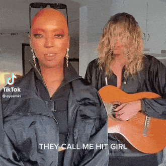 a man playing a guitar next to a woman with the words they call me hit girl on her face