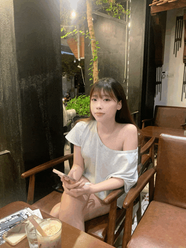 a woman sits at a table with her legs crossed holding a cell phone