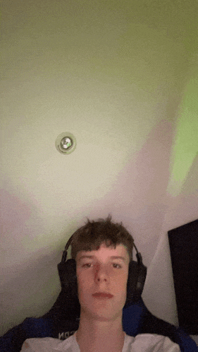 a young man wearing headphones looks at the camera with a light on the ceiling above him