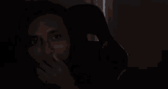a man is sitting in a chair in the dark and smiling with the words henehenehene behind him .