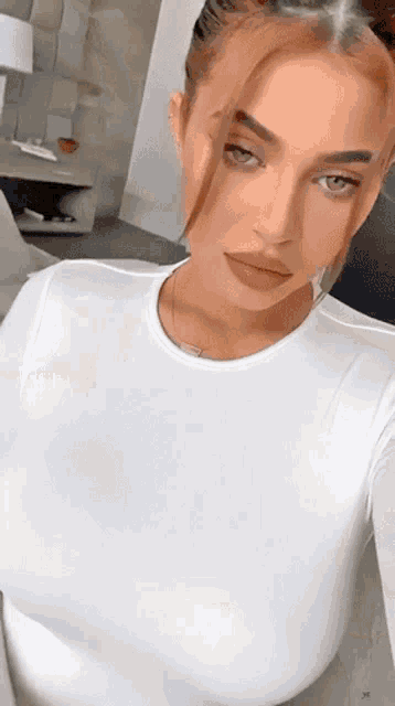 a woman in a white shirt is taking a selfie with her phone .