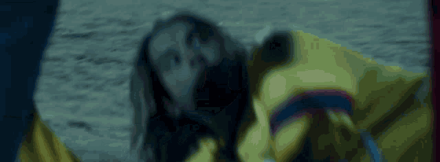 a woman in a yellow jacket is laying on the ground with her eyes closed .