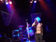 a man singing into a microphone on a stage with a drum set in the background