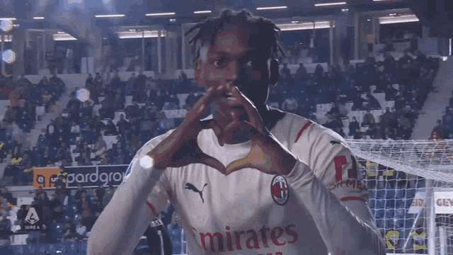a soccer player wearing a shirt that says emirates makes a heart with his hands