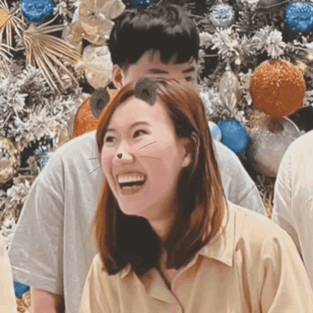 a woman with a cat nose is smiling in front of a christmas tree