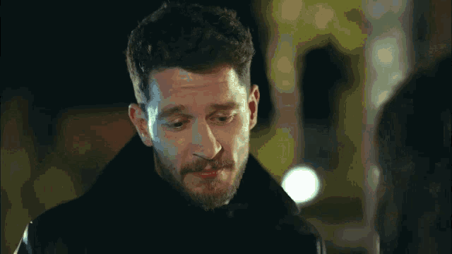a man with a beard is looking down at something while standing in front of a woman .