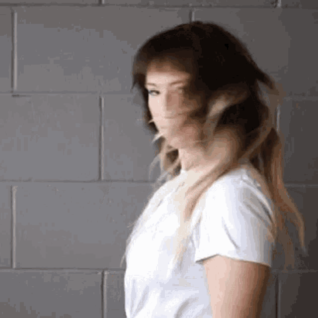 a woman in a white shirt is standing in front of a brick wall .