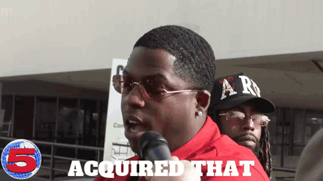 a man in a red shirt speaking into a microphone with the words acquired that below him