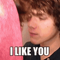 a young boy is standing in front of a pink curtain and says `` i like you '' .
