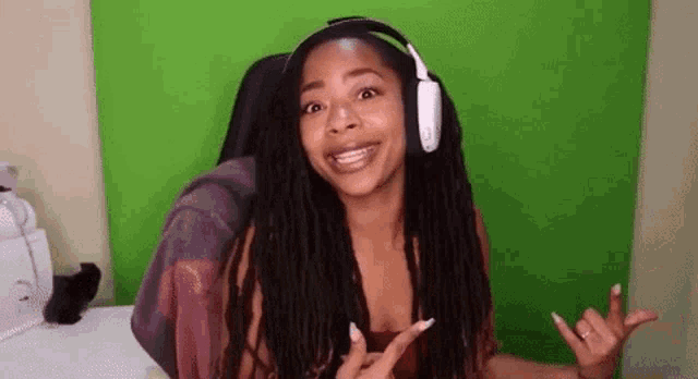 a woman wearing headphones is sitting in front of a green screen and making a funny face .