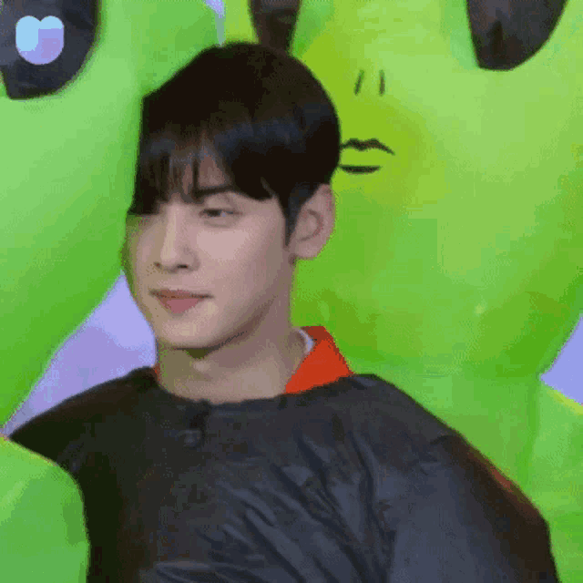 a man in a black jacket is standing in front of a green inflatable alien .