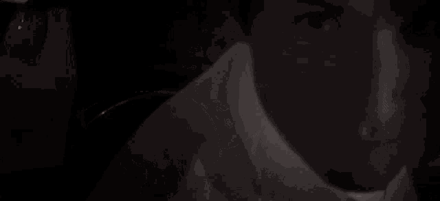 a close up of a man 's face in a dark room with a white shirt on .