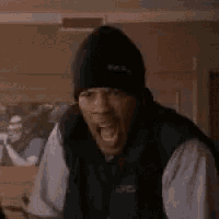 a man wearing a black beanie and a black vest is sitting in a living room .