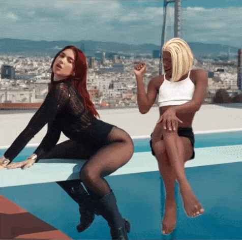 a man and a woman are sitting on the edge of a pool with a city in the background