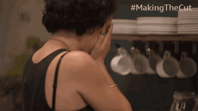a woman covering her face in front of a shelf of coffee cups and plates with the hashtag #makingthecut