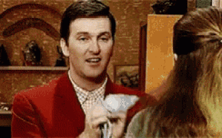 a man in a red suit is talking to a woman while holding a piece of paper .