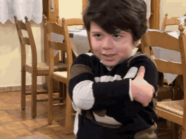 a young boy giving a thumbs up in a room with chairs