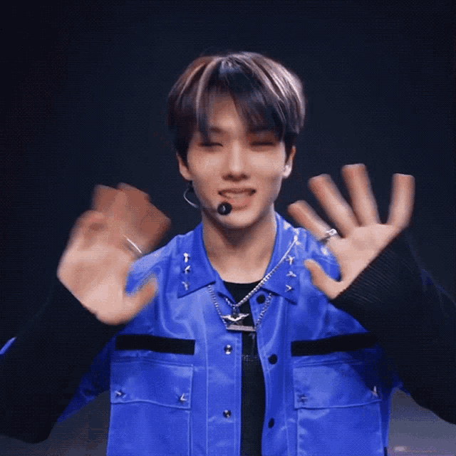 a young man wearing a blue jacket and black sweater is waving