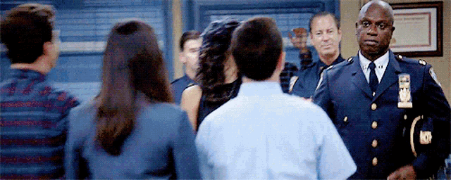 a group of people are standing in a room with a police officer standing in front of them .