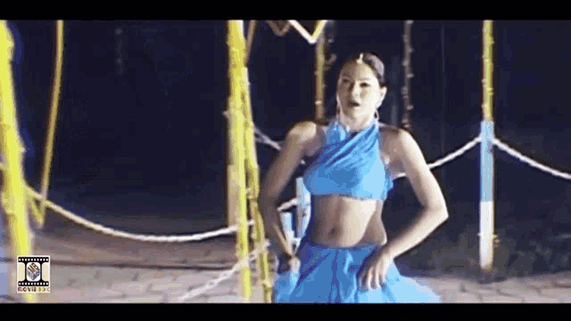 a woman in a blue crop top and blue skirt is dancing in a dark room .