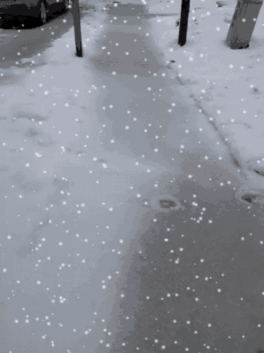 snow is falling on a sidewalk in front of a car