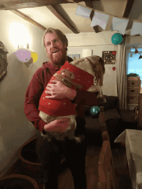 a man is holding a dog wearing a red sweater with a bear on it